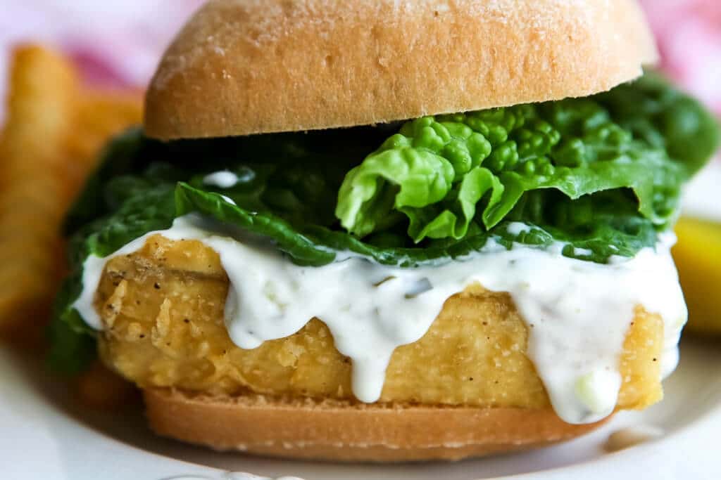 A vegan fish sandwich with tarter sauce and lettuce on it. 