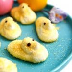 Yellow vegan peeps on a blue plate with colored Easter eggs behind it.