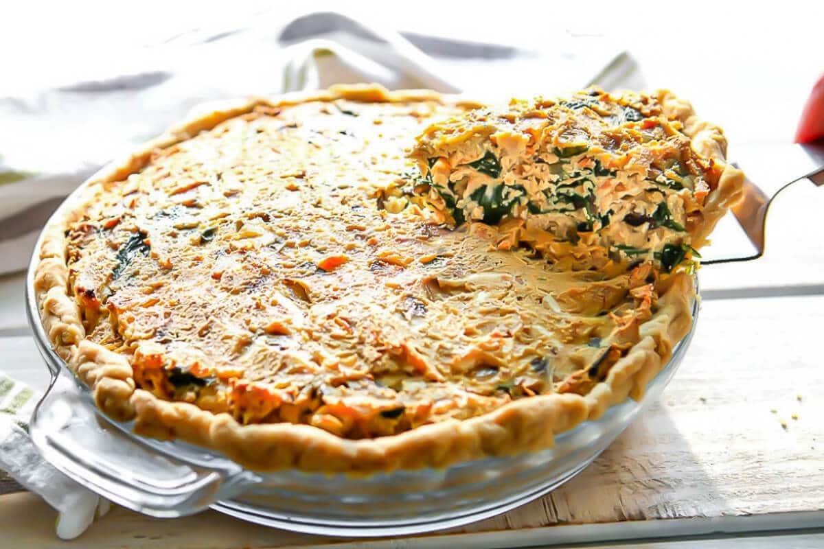 A pie dish full of tofu quiche with a slice being taken out of it.