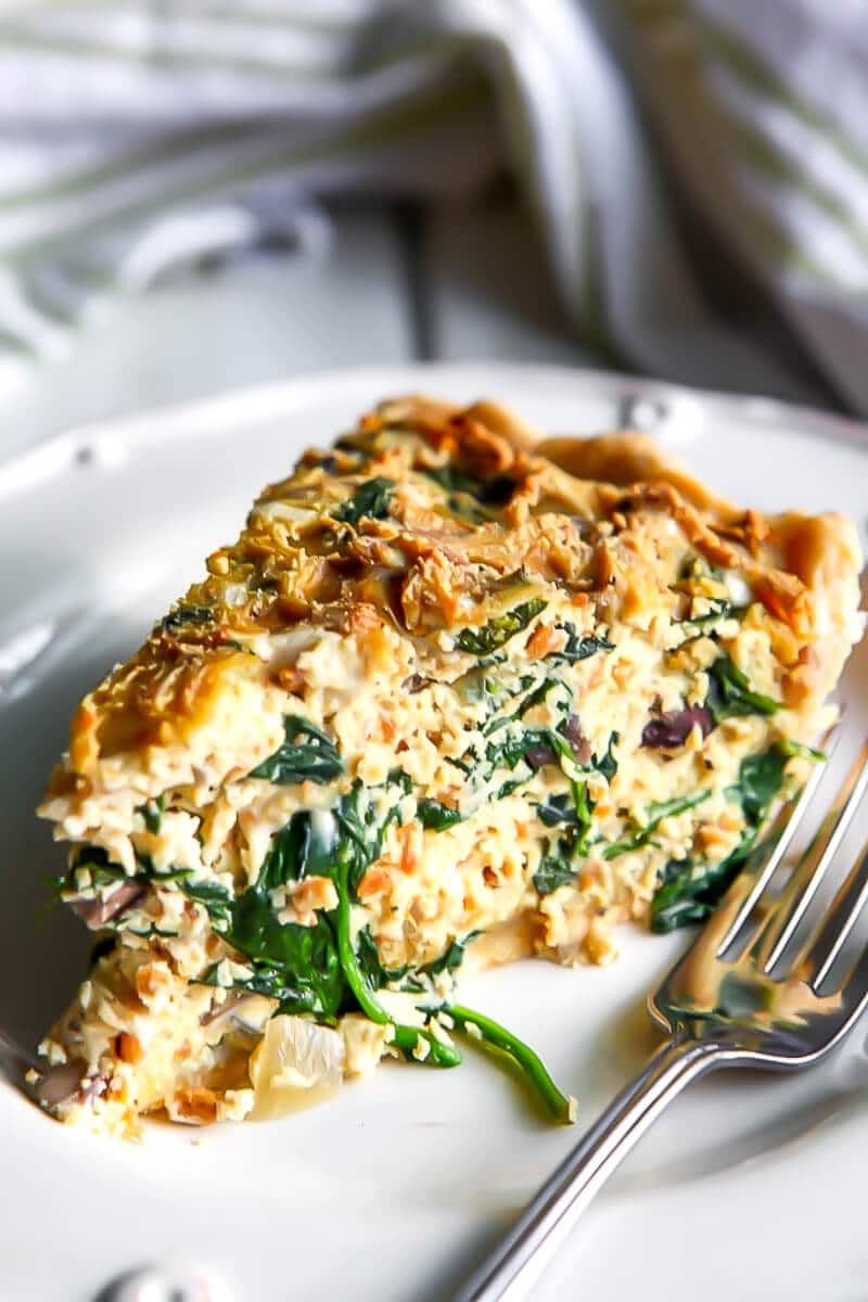 A white plate with a slice of a vegan quiche packed with spinach.