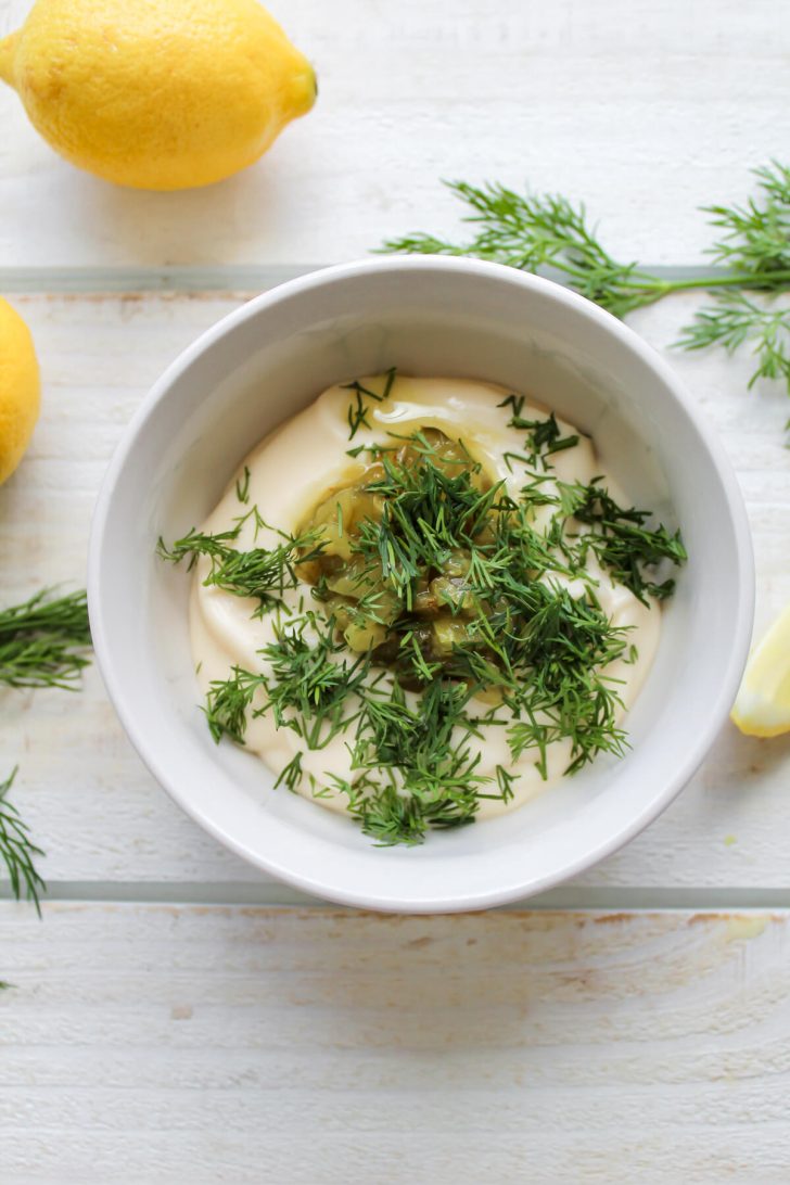 All of the vegan tartar sauce ingredients added to a small bowl with lemon and dill on the side.