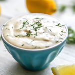 A small blue bowl filled with vegan tartar sauce with a lemon wedge on the side.