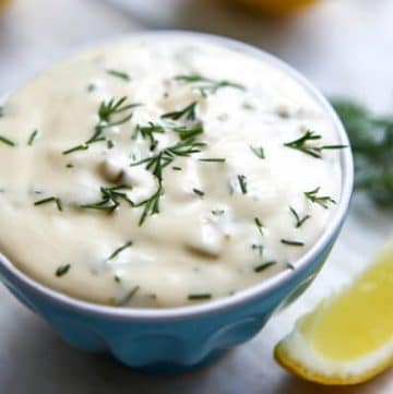 A small blue bowl filled with vegan tartar sauce with a lemon wedge on the side.