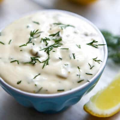 A small blue bowl filled with vegan tartar sauce with a lemon wedge on the side.