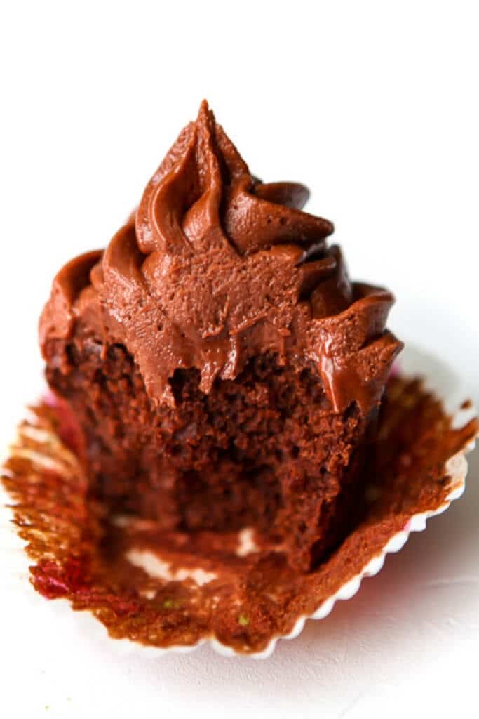 A chocolate cupcake with a bite taken out of it with chocolate frosting.