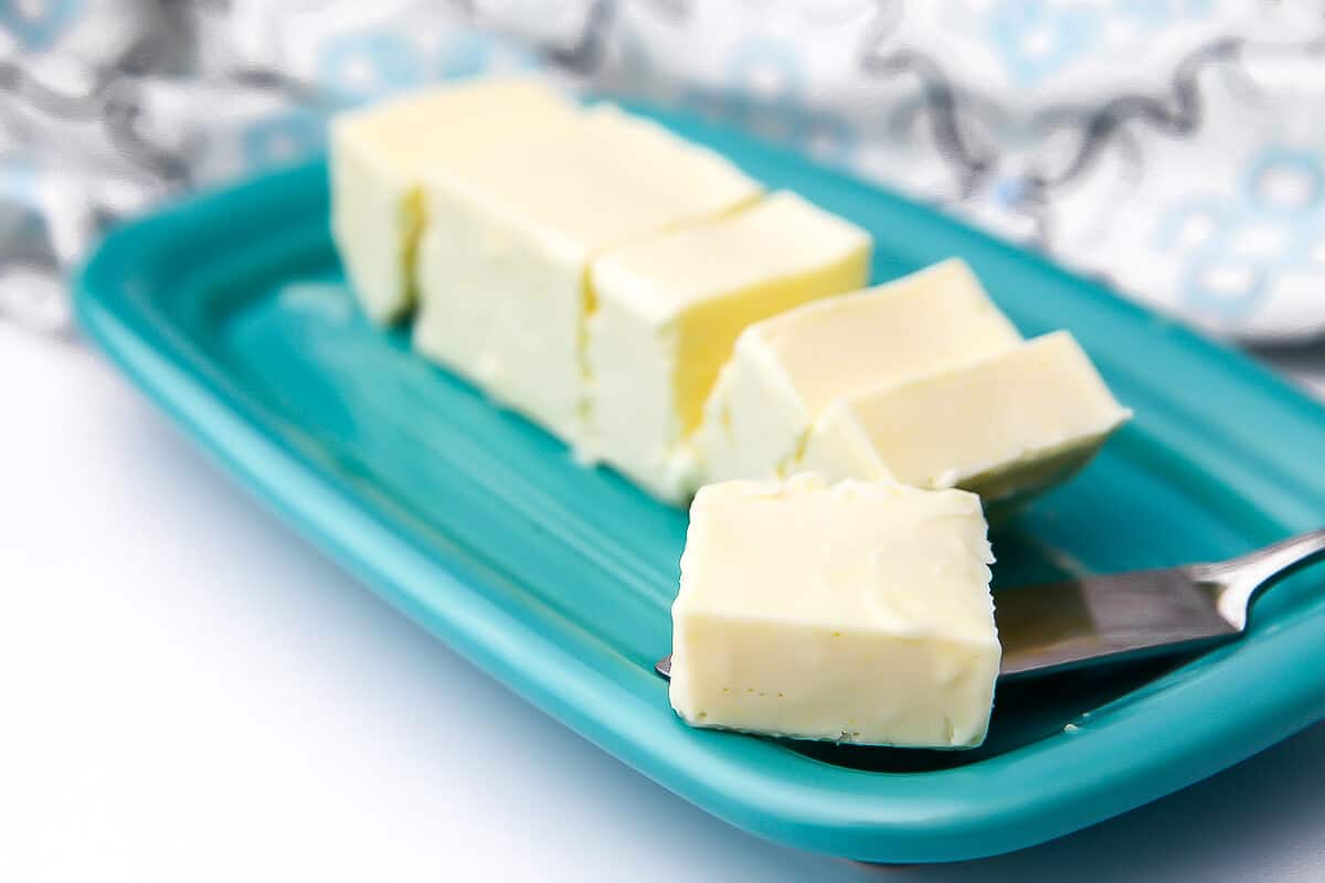 A stick of vegan butter on a blue butter dish with a pat of butter on a butter knife.