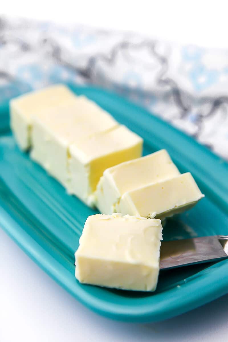 A blue butter dish with a stick of vegan butter cut into slices with a tea towel on the side.