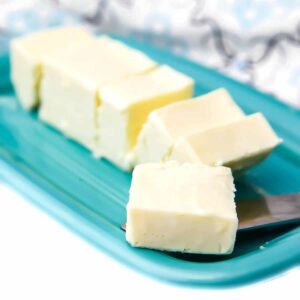 A stick of vegan butter on a blue butter dish cut into pieces with a piece on a butter knife.
