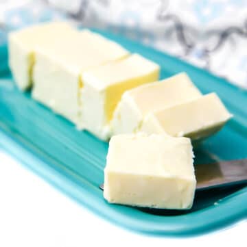 A stick of vegan butter on a blue butter dish cut into pieces with a piece on a butter knife.