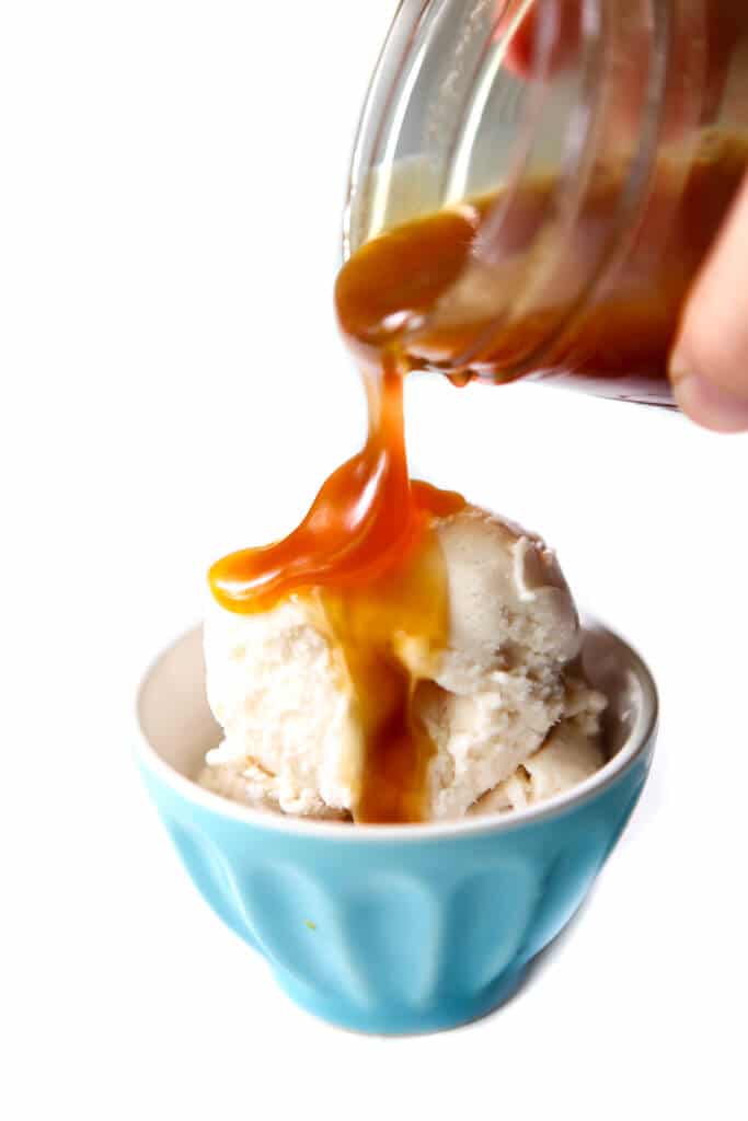Vegan butterscotch sauce being poured over vanilla vegan ice cream.