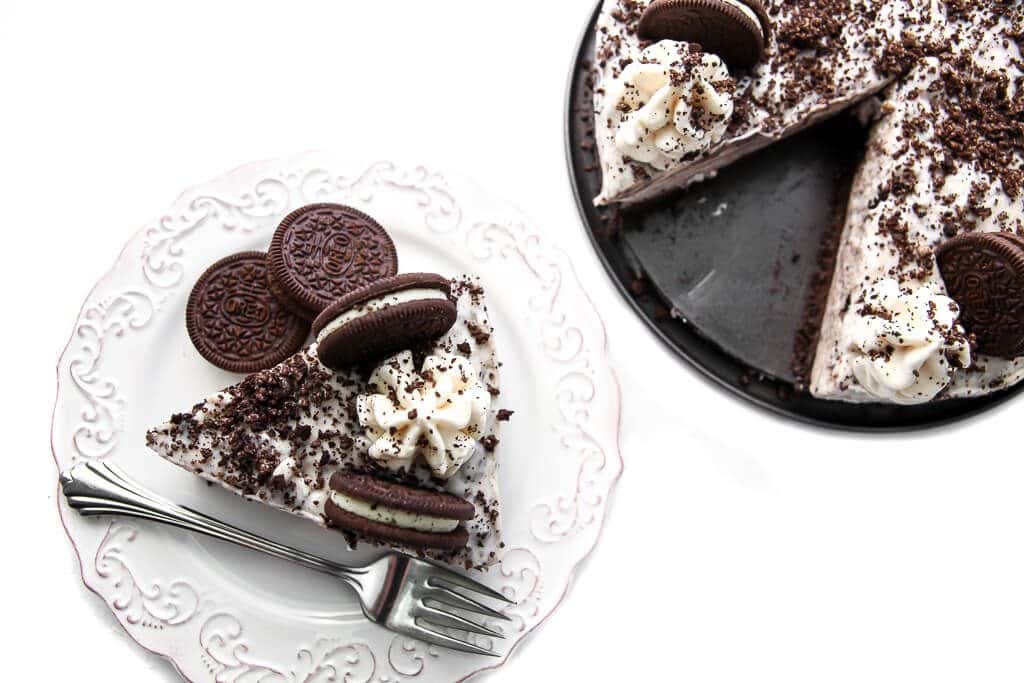 A vegan Oreo cheesecake with a slice taken out of it on a white plate. 