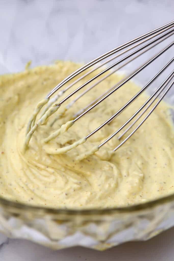 Creamy dressing in a bowl being blended with a hand held whisk.