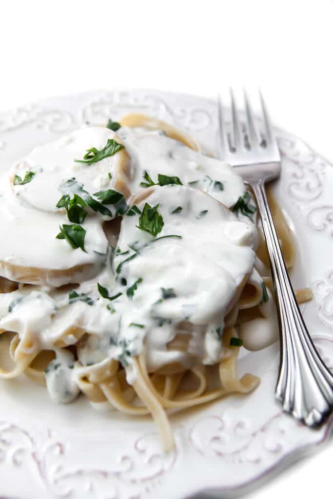 A white plate filled with linguine topped with vegan scallops and a garlic cream sauce garnished with parsley.