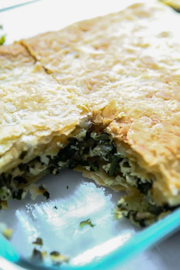 A baking dish filled with vegan spanakopita with a slice taken out of it. 