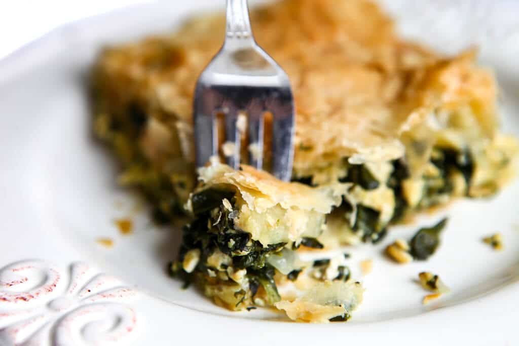 A piece of spinach pie with a fork taking a piece off of it.