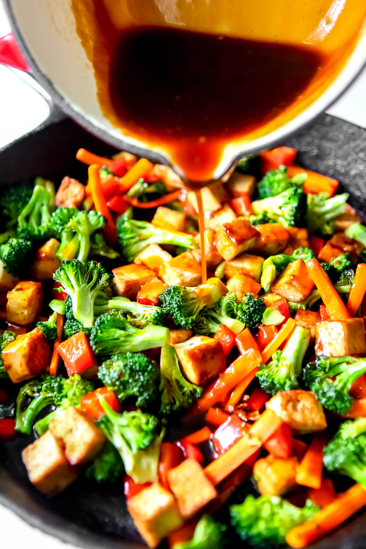 Teriyaki tofu with vegetables in a frying pan with teriyaki sauce being poured over it.