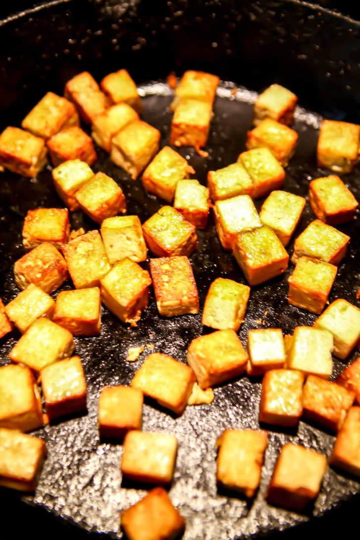Cubes of tofu frying in an iron skillet.