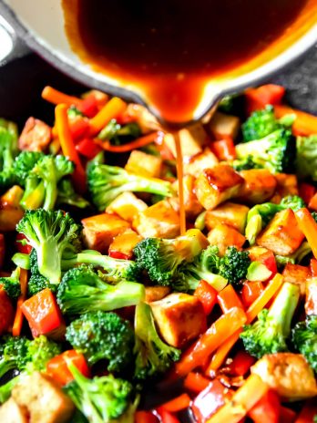Teriyaki tofu with vegetables in a frying pan with teriyaki sauce being poured over it.