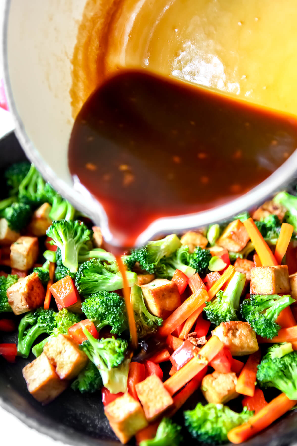 Teriyaki sauce being poured over stir-fried vegetables and fried tofu.