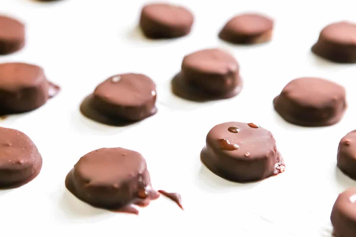 Frozen chocolate covered banana bites on white parchment paper.