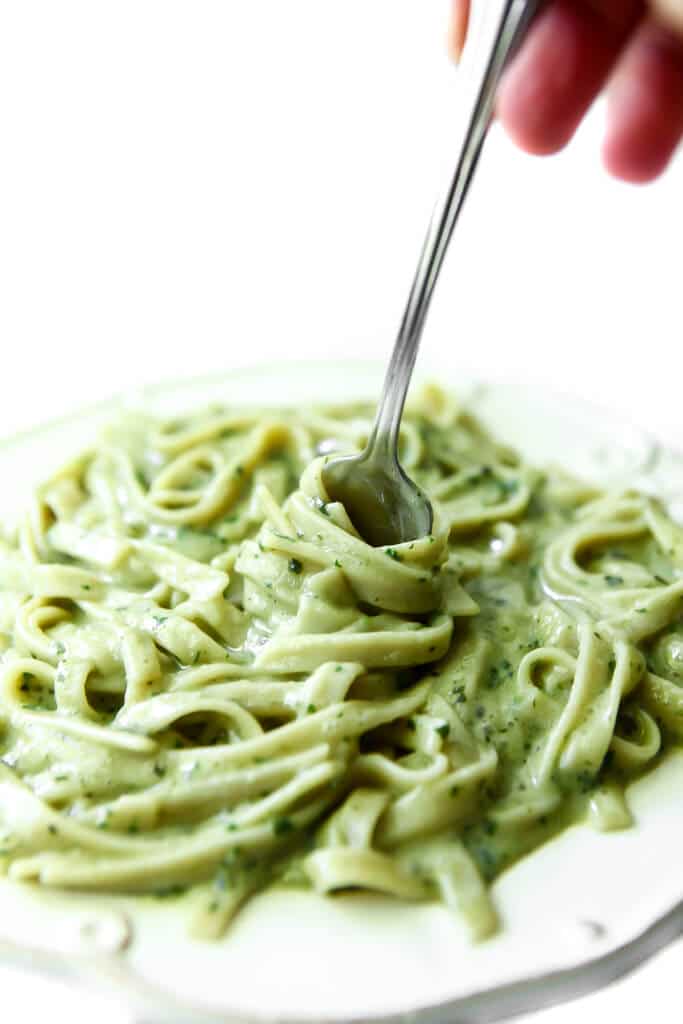A fork twirling pasta with a vegan pesto sauce on it. 