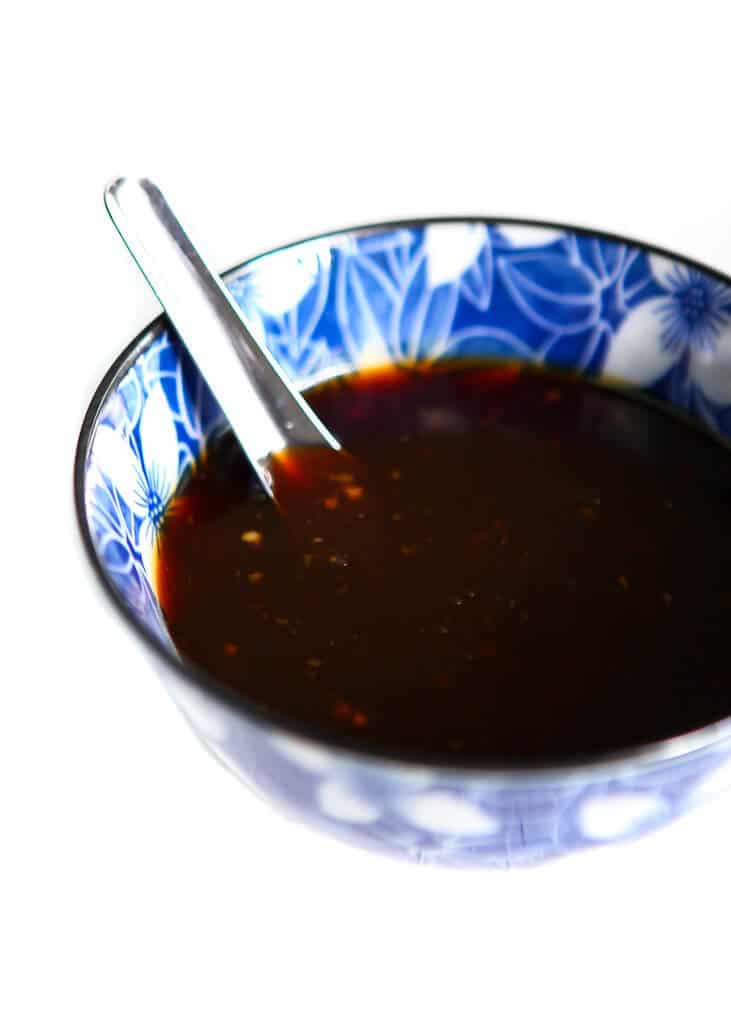 A blue bowl filled with teriyaki sauce with a spoon in it.