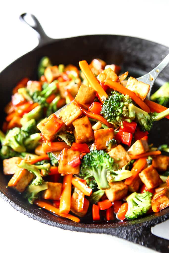 An iron skillet filled with sauted veggies and teriyaki tofu.