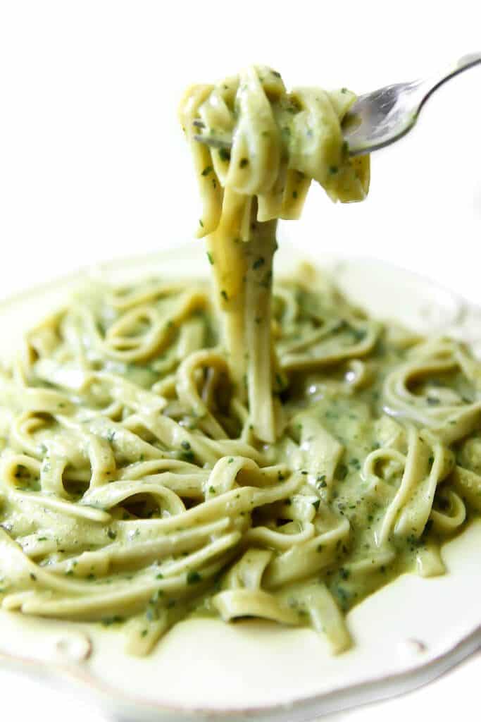 A plate filled with creamy vegan pesto sauce over pasta and a fork full of the pasta over the dish.