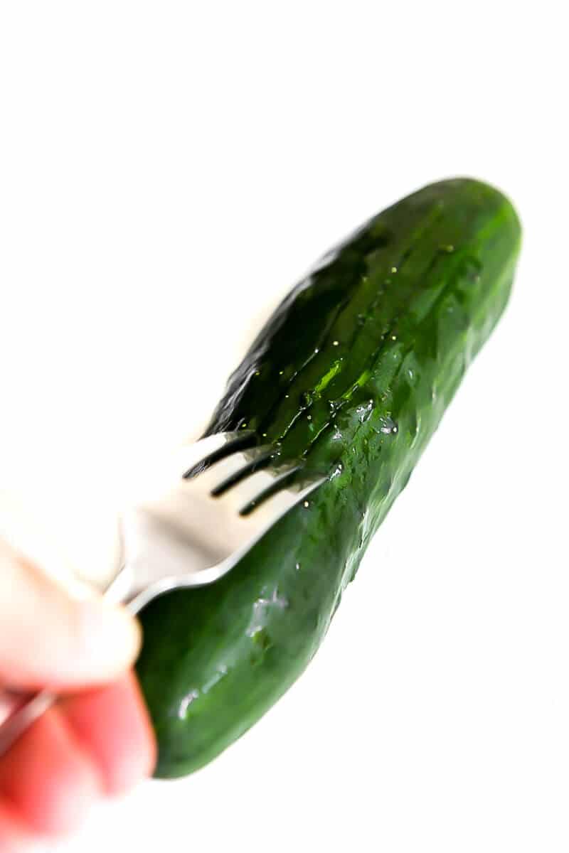 Scoring the sides of a cucumber with a fork before cutting for refrigerator pickles.
