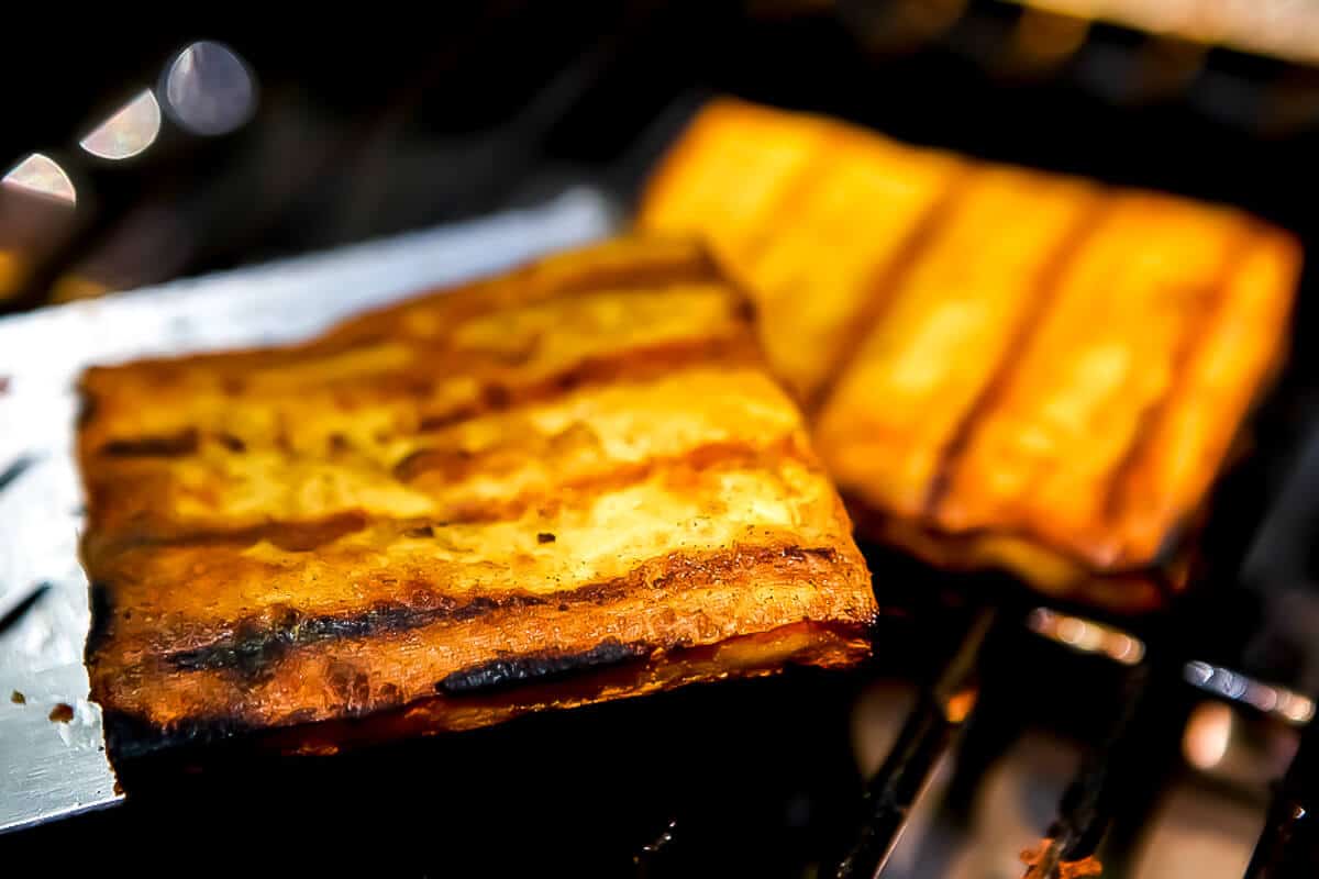 A tofu steak being taken off the grill with a spatula.