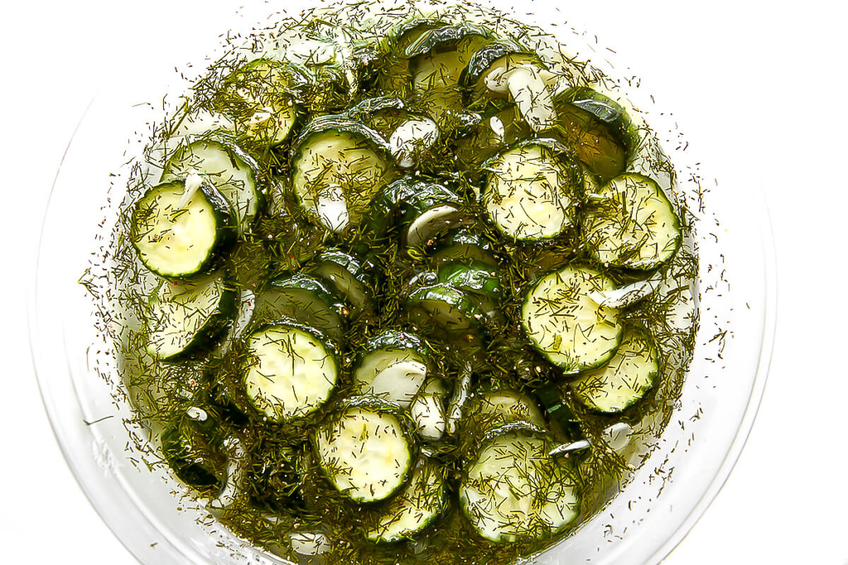 A big glass bowl filled with refrigerator pickles marinating in brine.