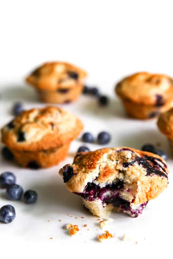 Gluten-free blueberry muffins on white parchment with a bite taken out of a muffin.