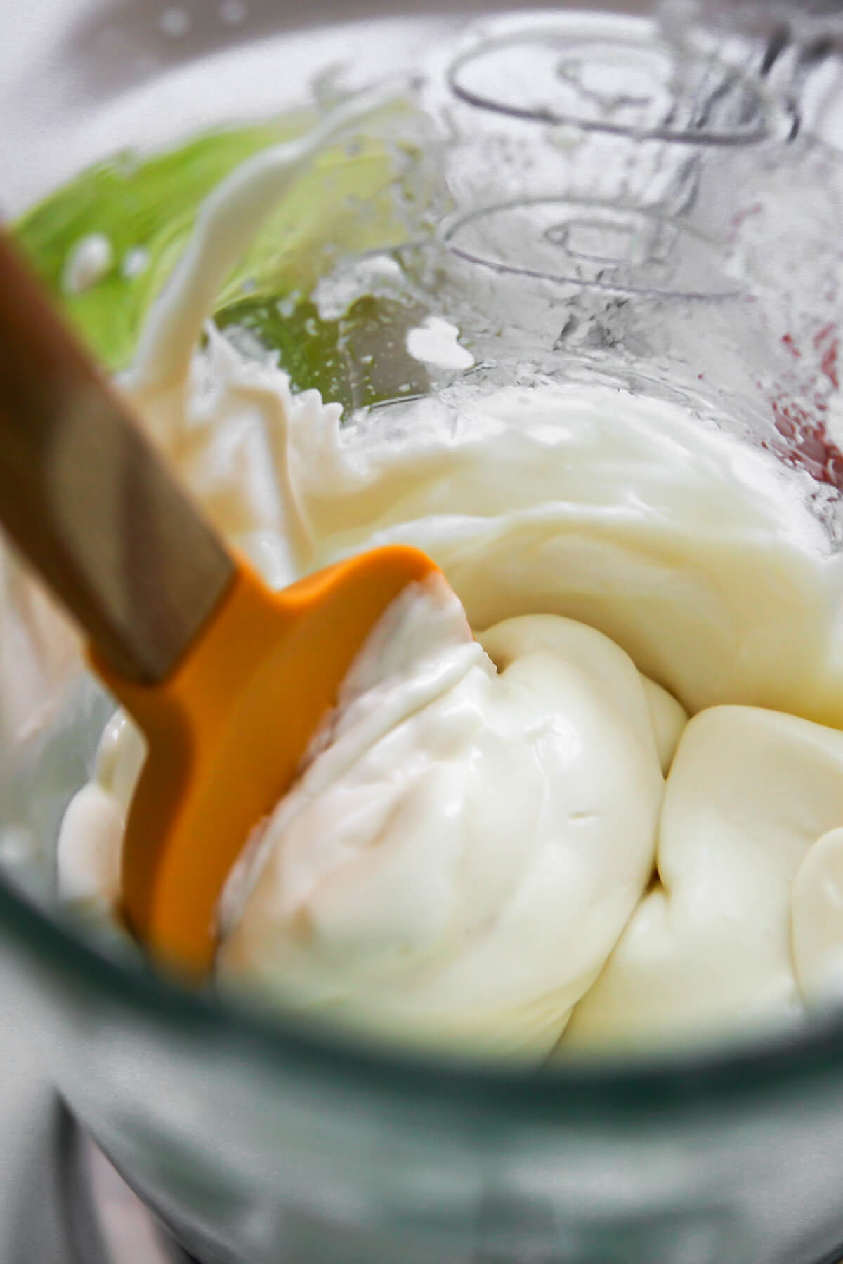 Vegan mayo in a blender being scooped out with a rubber spatula.