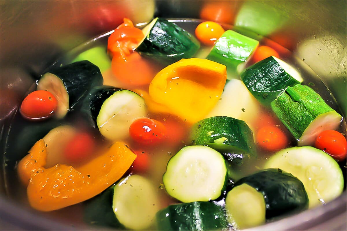 A soup pot filled with zucchini, bell pepper, tomatoes, and potatoes, with water just barely covering them.