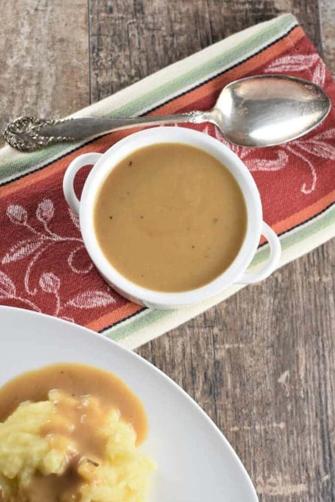 Gravy thickened with chickpea flour in a gravy boat with a plate of mashed potatoes and gravy.