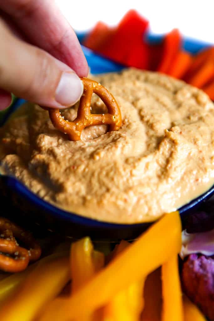 A gluten-free pretzel being dipped into vegan cashew cheese dip.
