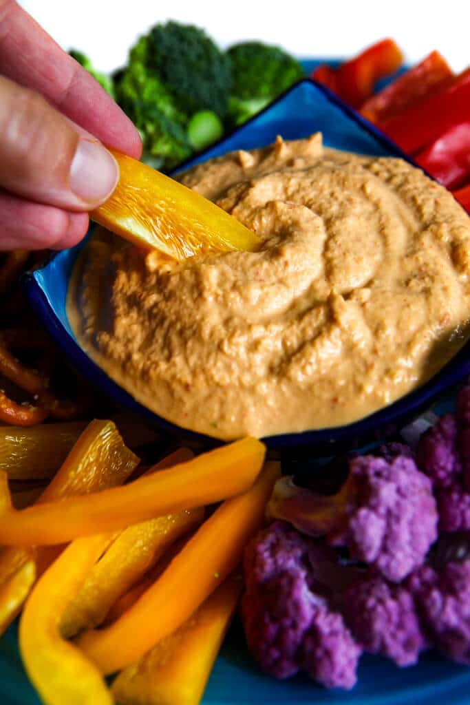 A bowl filled with cashew cheese dip with a yellow pepper being dipped into it.