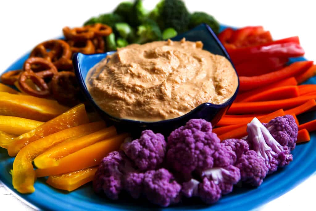 A blue plate filled with cashew dip with colorful vegetable all around it.