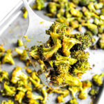 A cookie sheet filled with baked broccoli with a spatula holding up some of it.