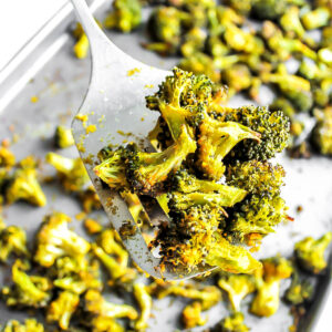 A cookie sheet filled with baked broccoli with a spatula holding up some of it.