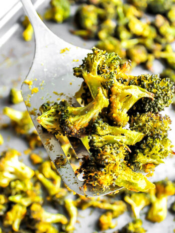 A cookie sheet filled with baked broccoli with a spatula holding up some of it.