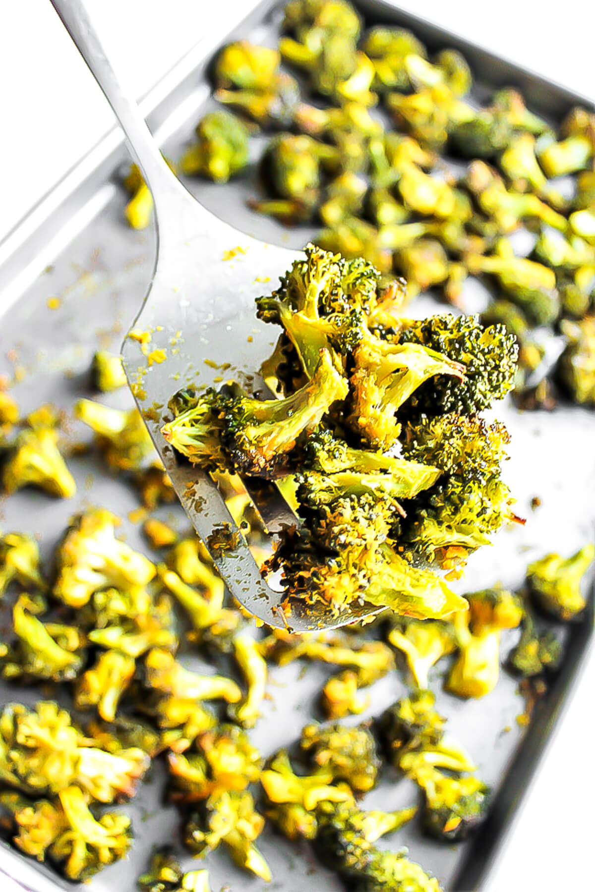A cookie sheet filled with baked broccoli with a spatula holding up some of it.