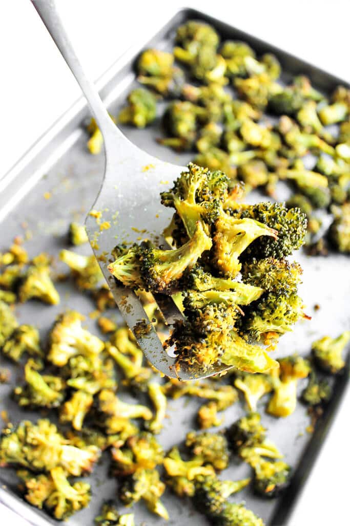 A cookie sheet filled with baked broccoli with a spatula holding up some of it.
