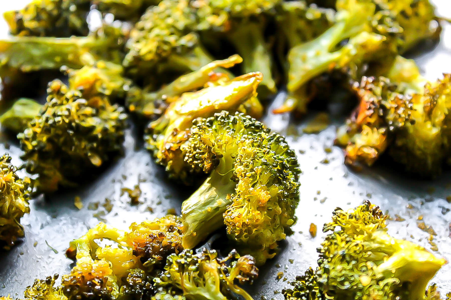 A close up of baked broccoli on a cookie sheet.