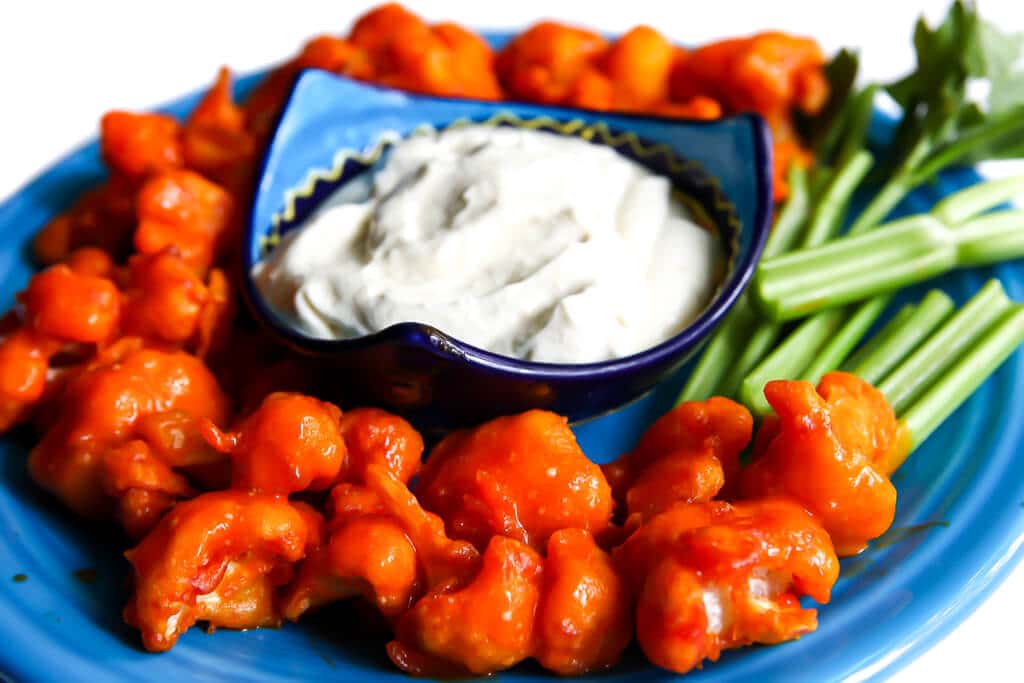 Vegan buffalo cauliflower nuggets on a blue plate with celery and vegan blue cheese dressing for dipping.