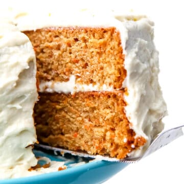 A close up of a carrot cake with vegan cream cheese frosting being served from a round cake.