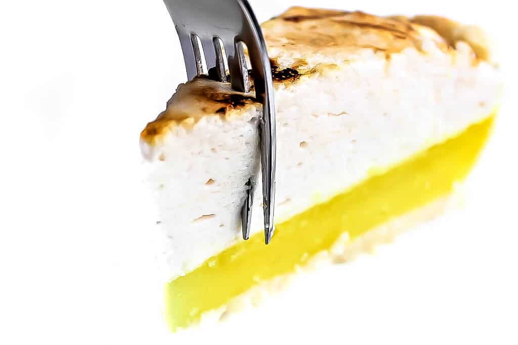A slice of vegan lemon meringue pie with a fork in it.