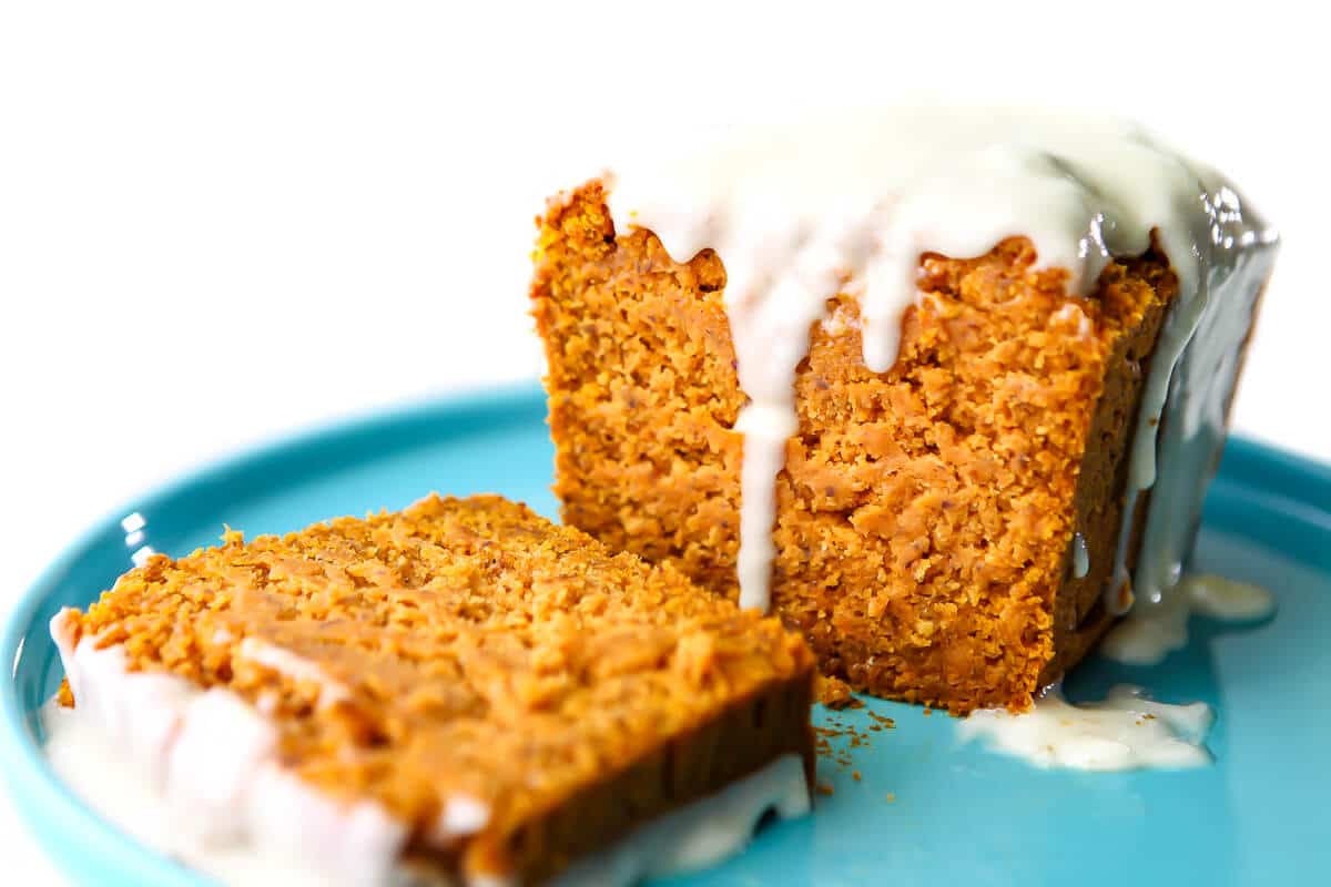 A loaf of vegan pumpkin bread with cream cheese frosting on top and dripping down the sides.