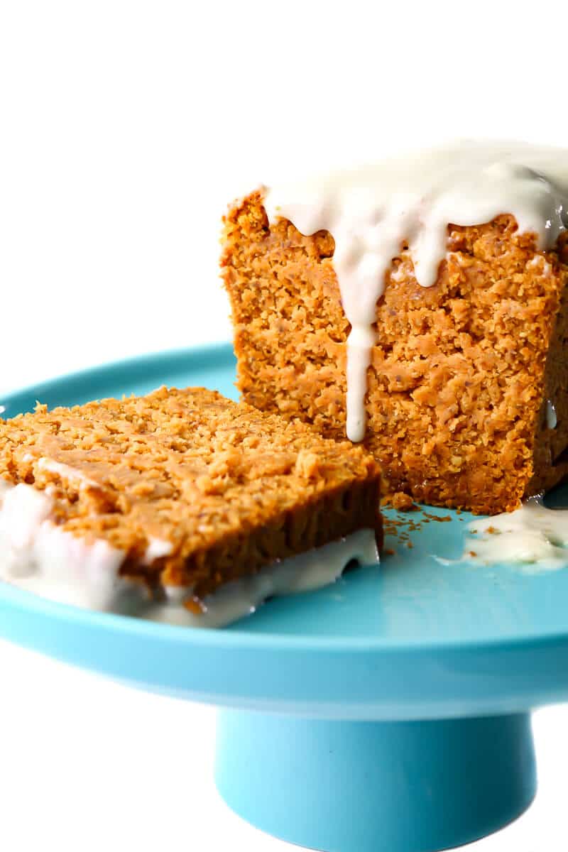 A loaf of vegan pumpkin bread with vegan cream cheese frosting on a blue cake pan.