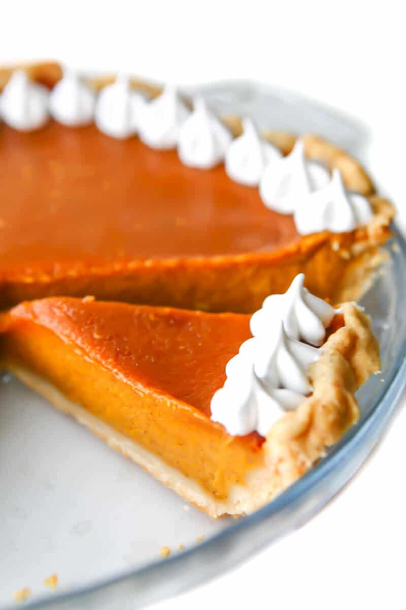 An egg-free pumpkin pie with whipped cream on top in a pie dish with a slice taken out.